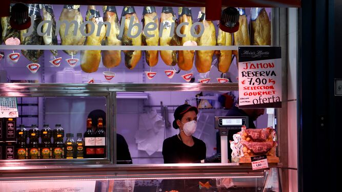 Una mujer atiende, con mascarilla, su puesto en un mercado de abastos de Córdoba.